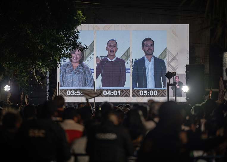 La gente observa en una pantalla gigante a los tres candidatos presidenciales / AFP